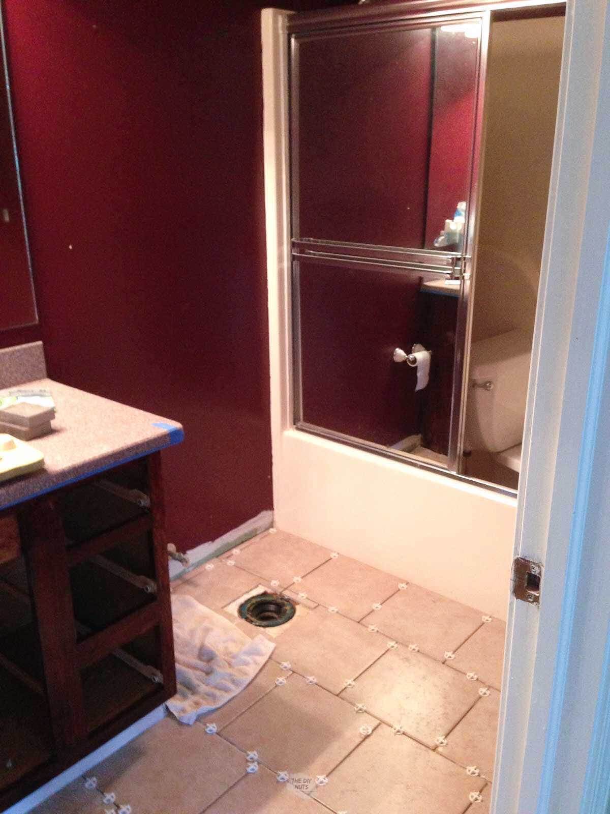 dark red walls, glass shower door with new tile being put down in bathroom.
