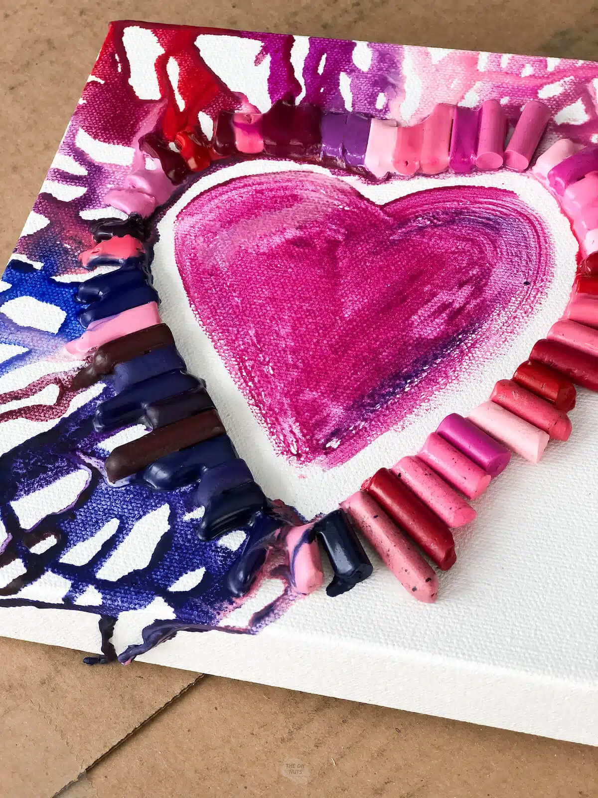 heart painted on canvas with crayons melted partially around the heart.