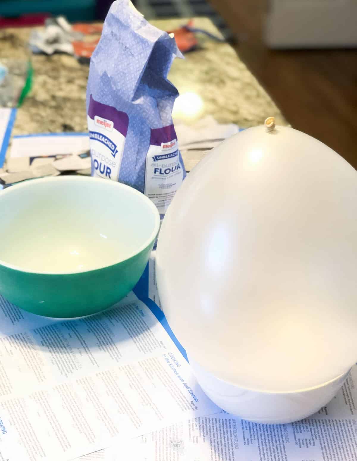 balloon in bowl with mixing bowl and flour on countertop.