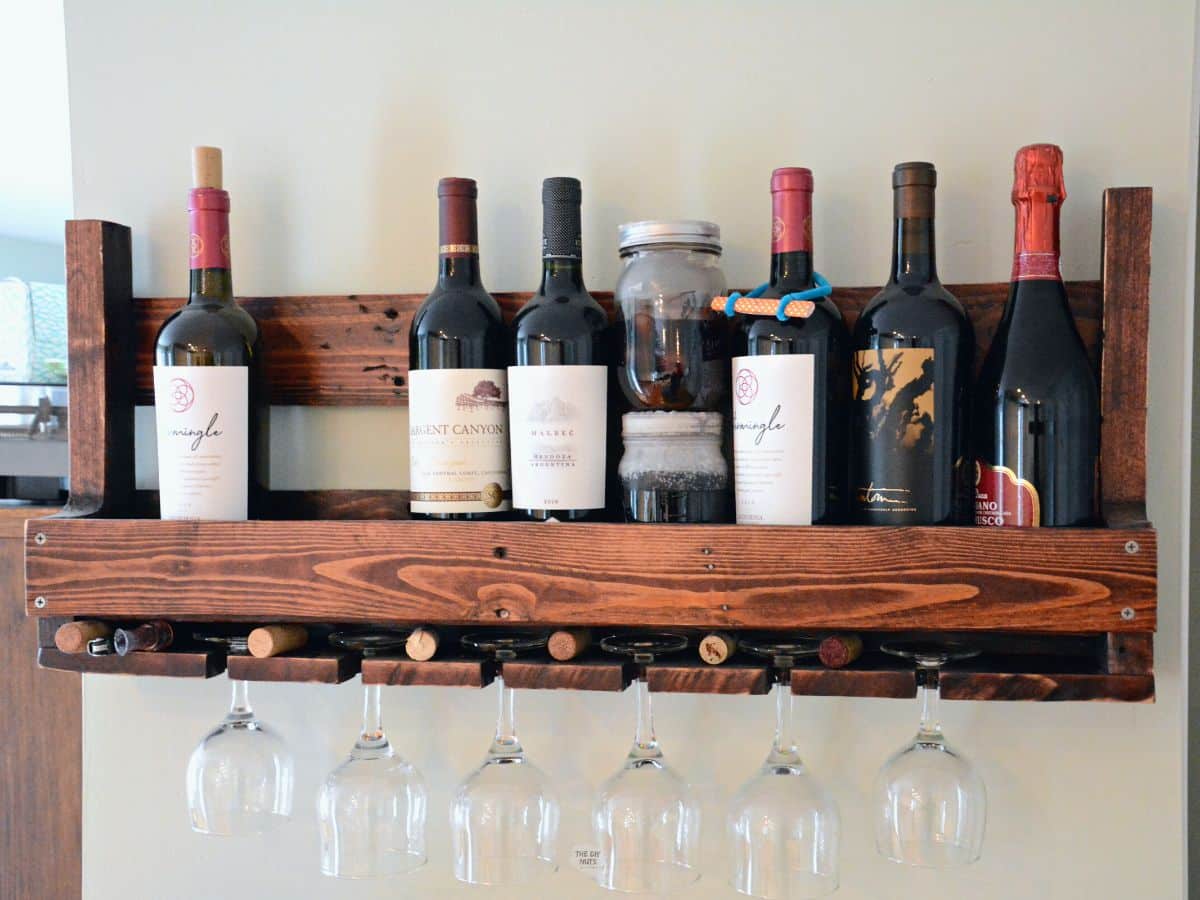front view of pallet wood wine rack with wine bottles and glasses hanging.