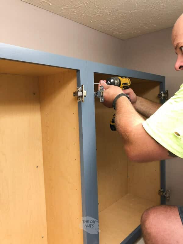 Man drilling painted cabinets horizontally to attach laundry cabinets