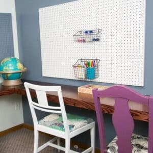 white pegboard on wall with two chairs and desk.