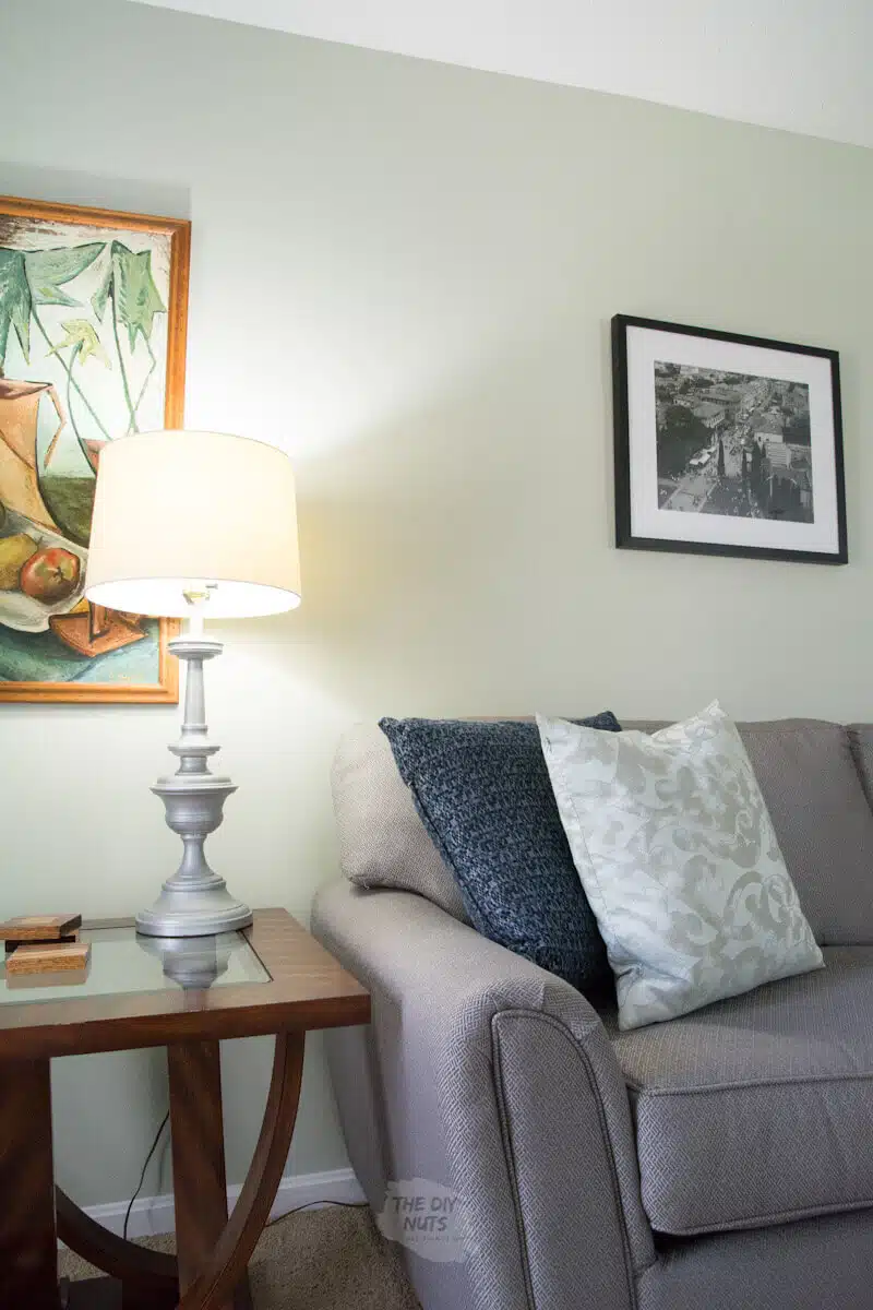 lamp on with painting and gray couch and liveable green painted walls