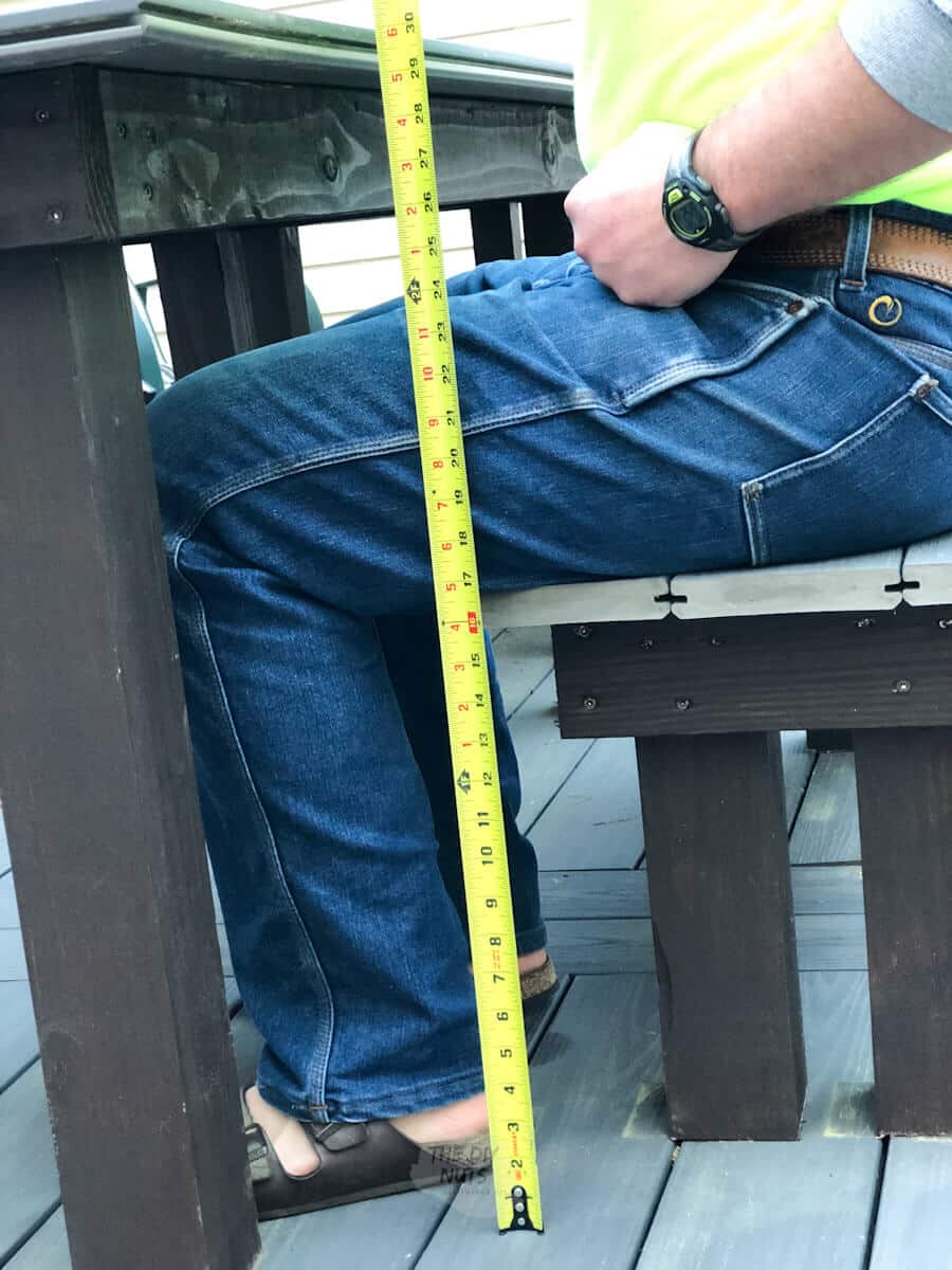 man holding tape measurer show height of bench, him sitting and outdoor table