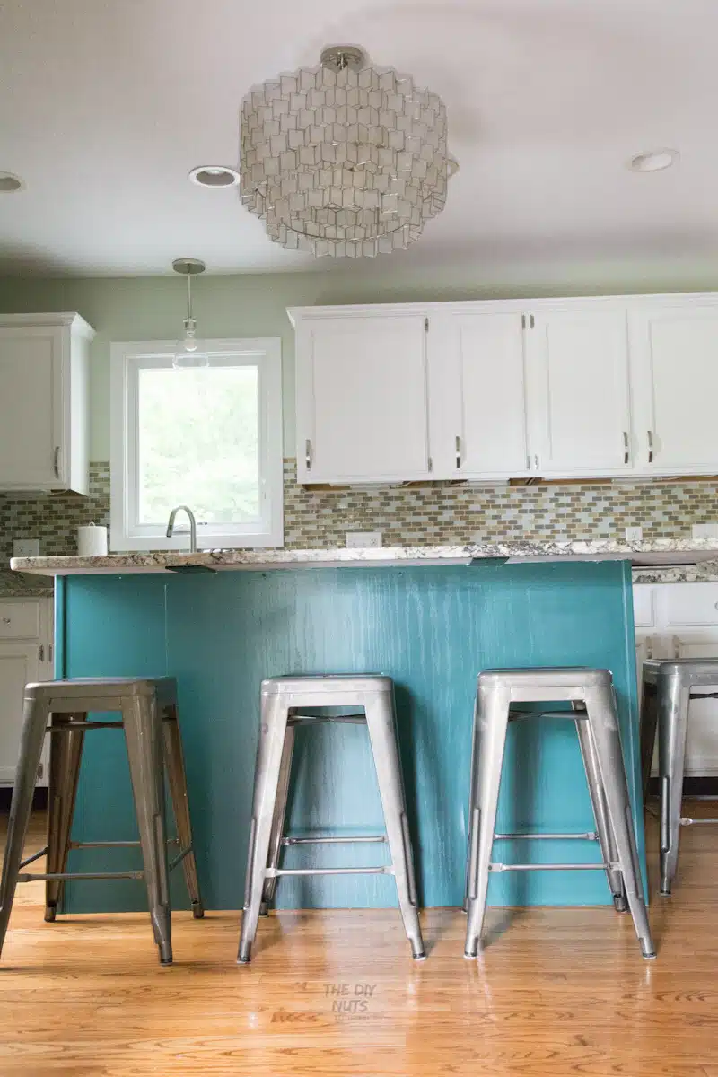 Painted Blue green kitchen island cabinets with metal bar stools and white upper cabinets.