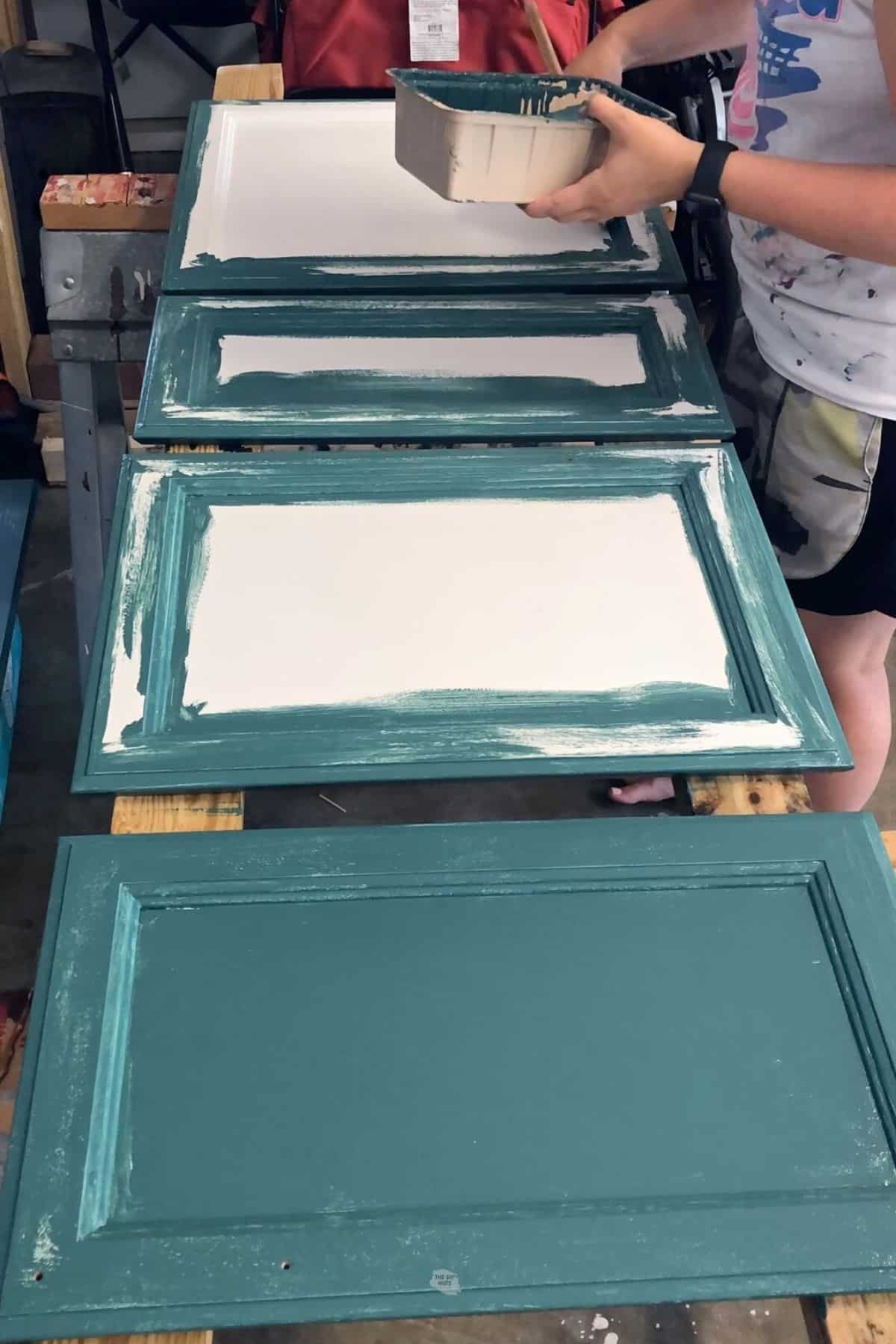 woman holding small paint tray using brush to paint cabinet doors.