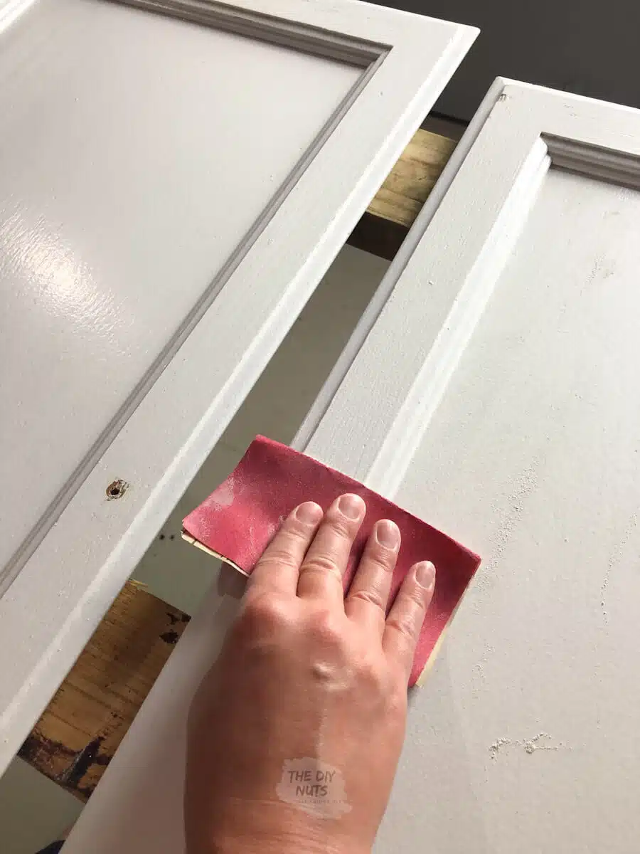 hand using 220 sandpaper before painting cabinets