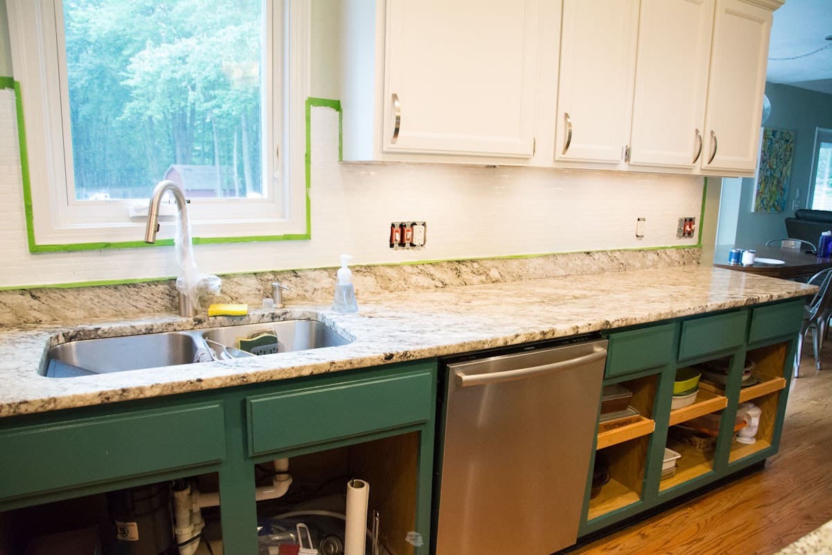 painted white tile backsplash with painter's tape around edges and white and green painted cabinets.