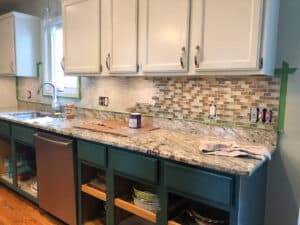 partially painted backsplash in kitchen with white and green cabinets.