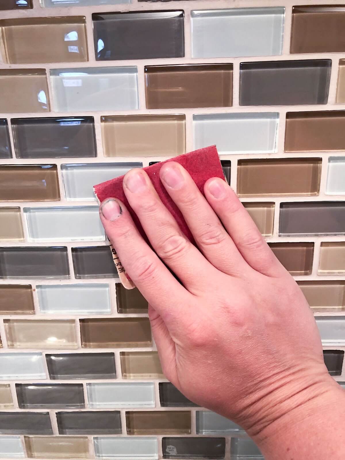 hand using sandpaper on glass mosaic tile.