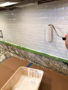 small roller applying white paint to backsplash.