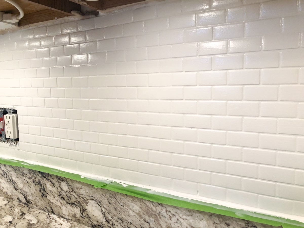 white painted backsplash tiles with green painter's tape along kitchen counter.