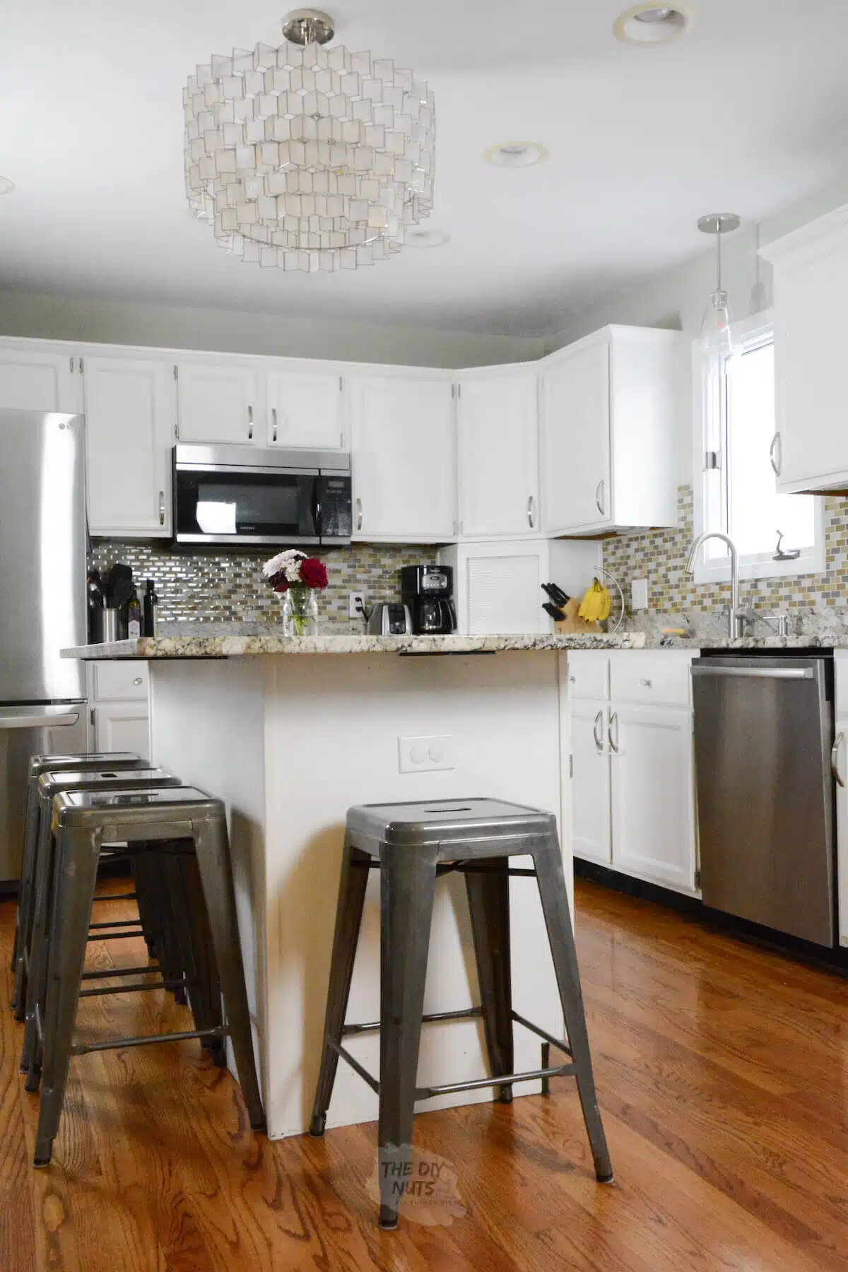 painted white kitchen cabinets with glass mosaic backsplash and capiz shell chandelier.