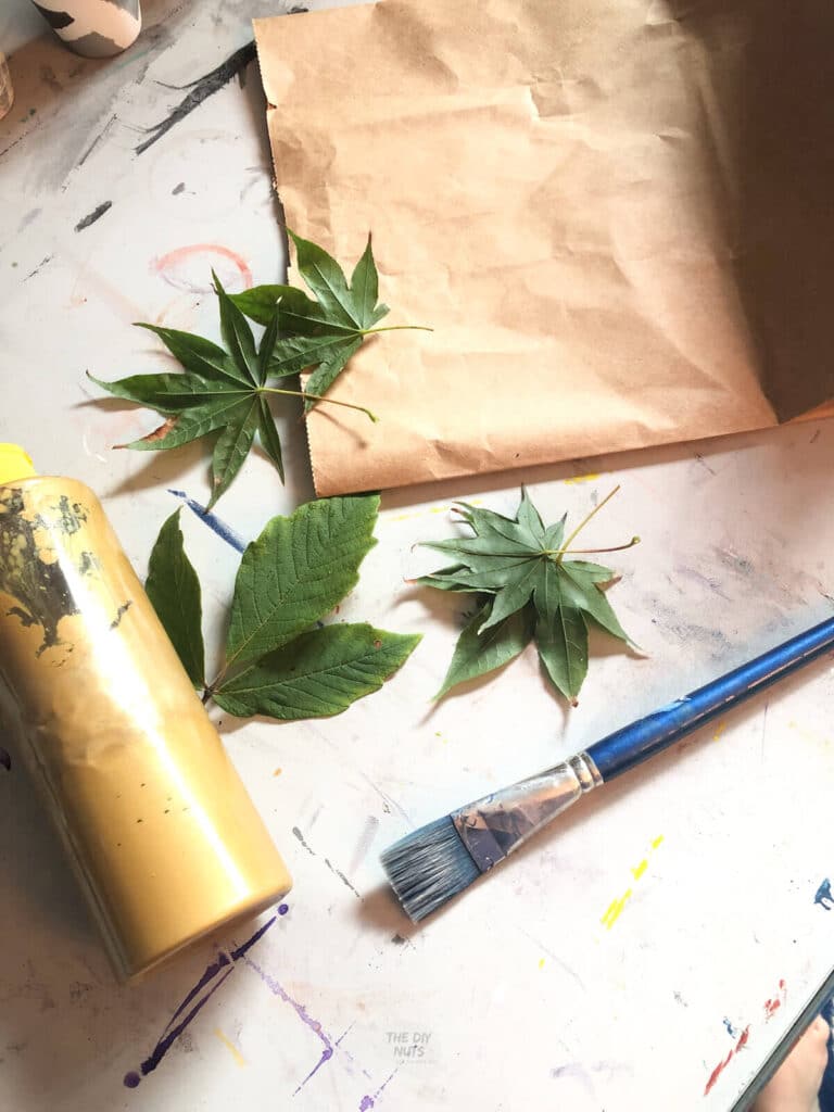 leaves, gold paint, paintbrush and brown paper bag used for eco-friendly DIY wrapping paper