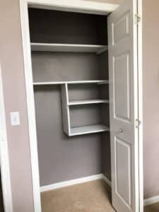 gray closet with white wooden shelves with door open.
