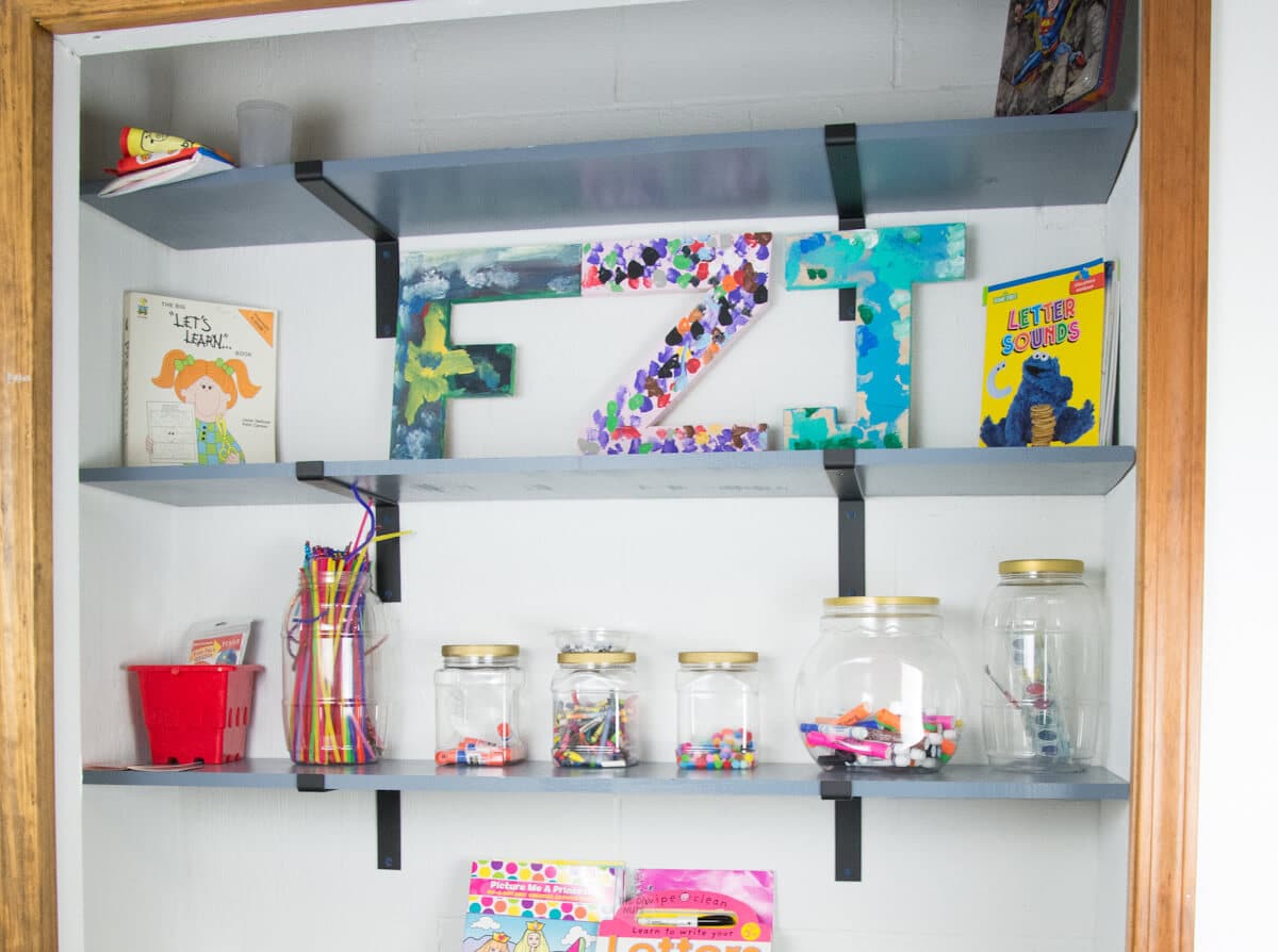craft closet with wood shelves on brackets displaying painted letters and craft supplies.
