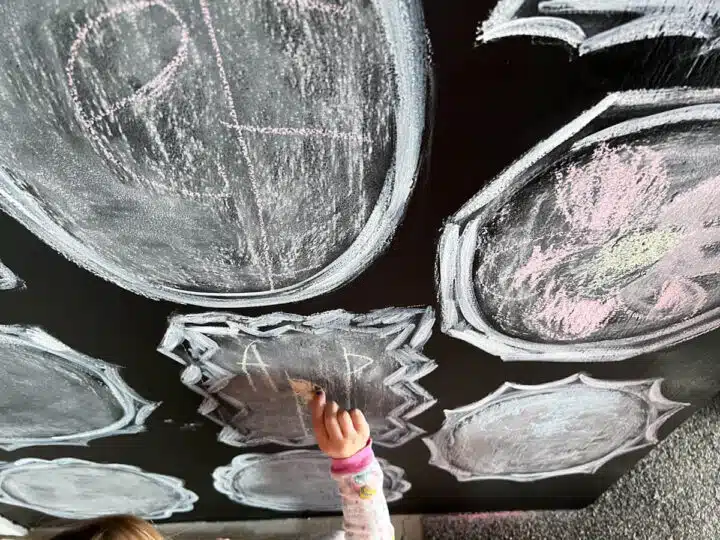 child's hand using chalk on a chalkboard mural