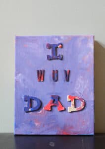 purple and red painted canvas by kids with wooden letters on it that say I wuv dad.