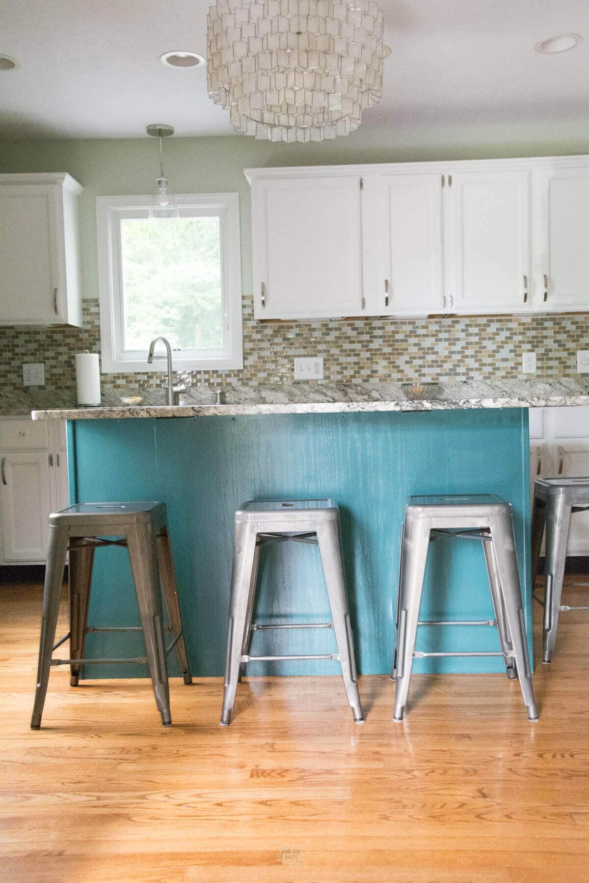 blue green painted kitchen island with metal bar stools and white painted kitchen cabinets.
