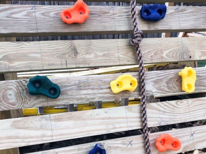 orange, blue, yellow rock wall holds on DIY climbing wall on DIY playset with rope.