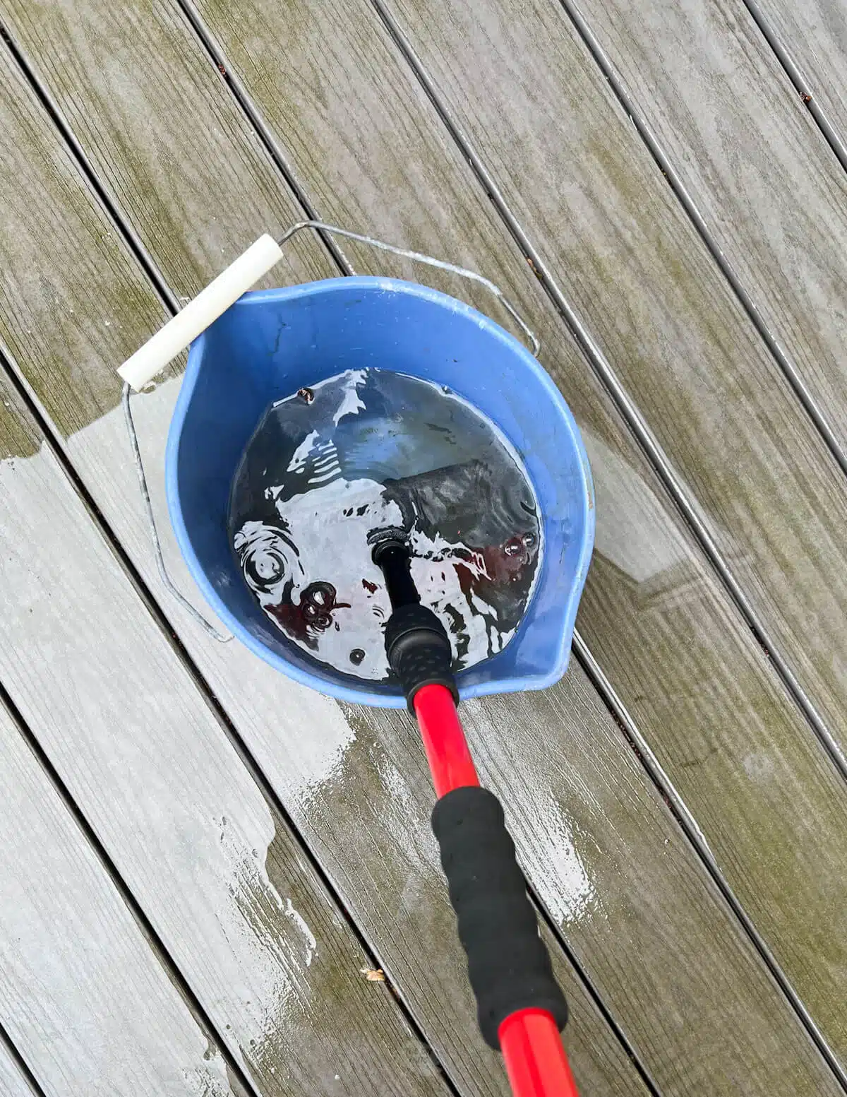 deck brush being put in DIY cleaning solution in blue bucket.