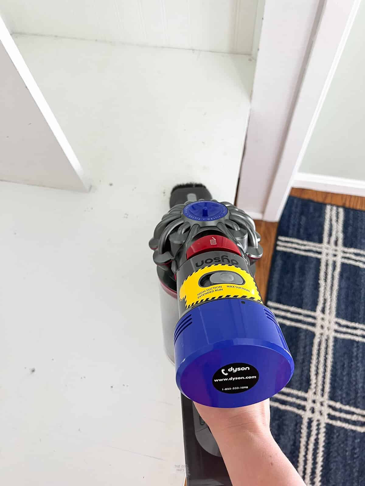 hand holding dyson vacuum cleaning wood shelves.