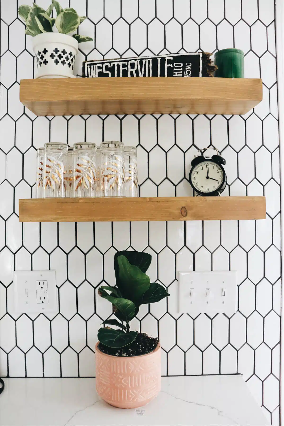 geometric white backsplash tile with oak open floating shelves and accessories.