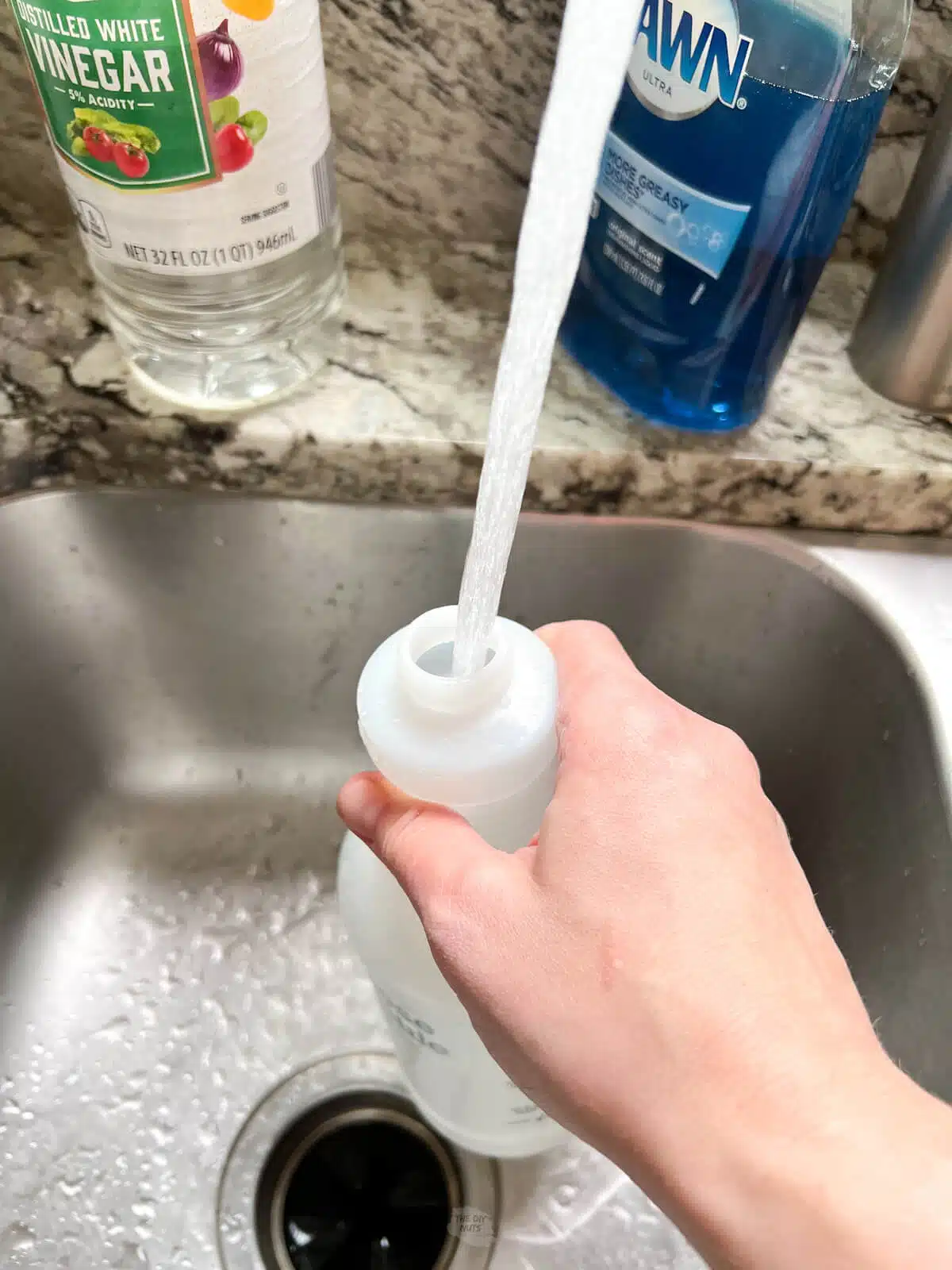 hand holding empty spray bottle making homemade cleaner with vinegar.