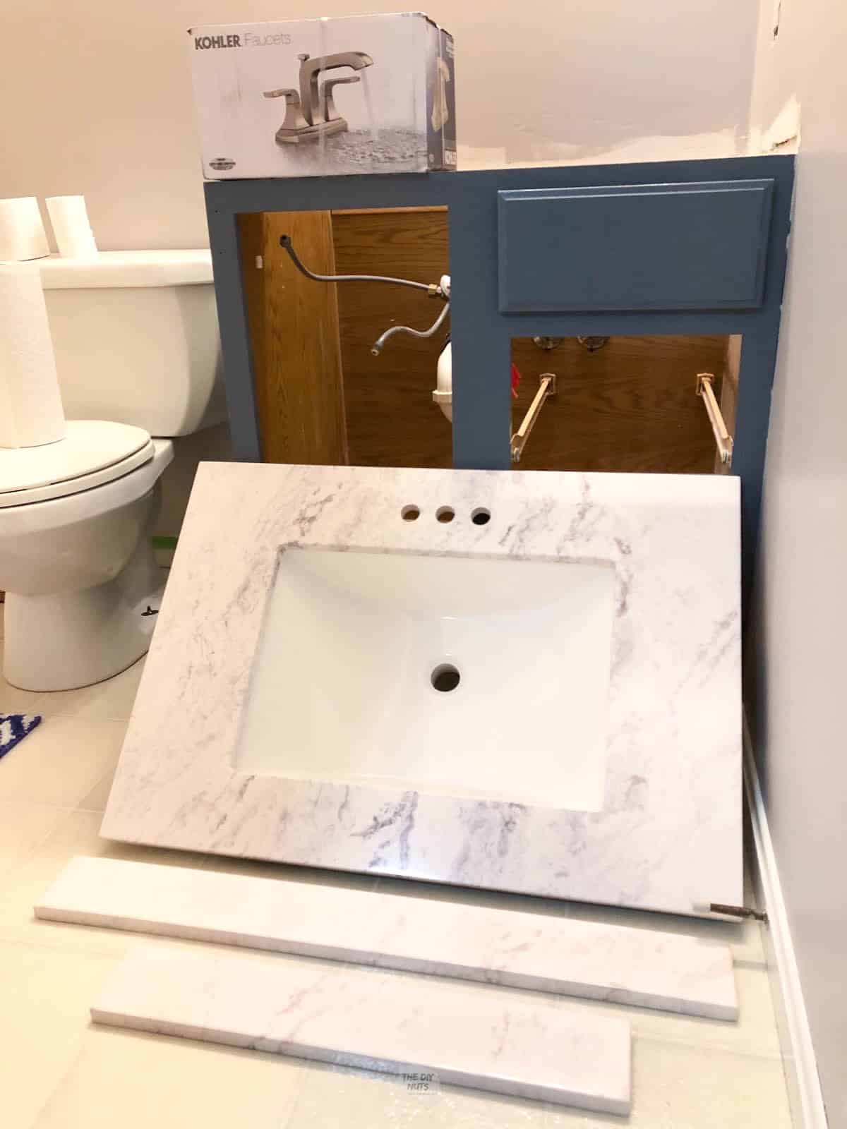 premade marble counter sitting on floor in front of painted bathroom cabinet.