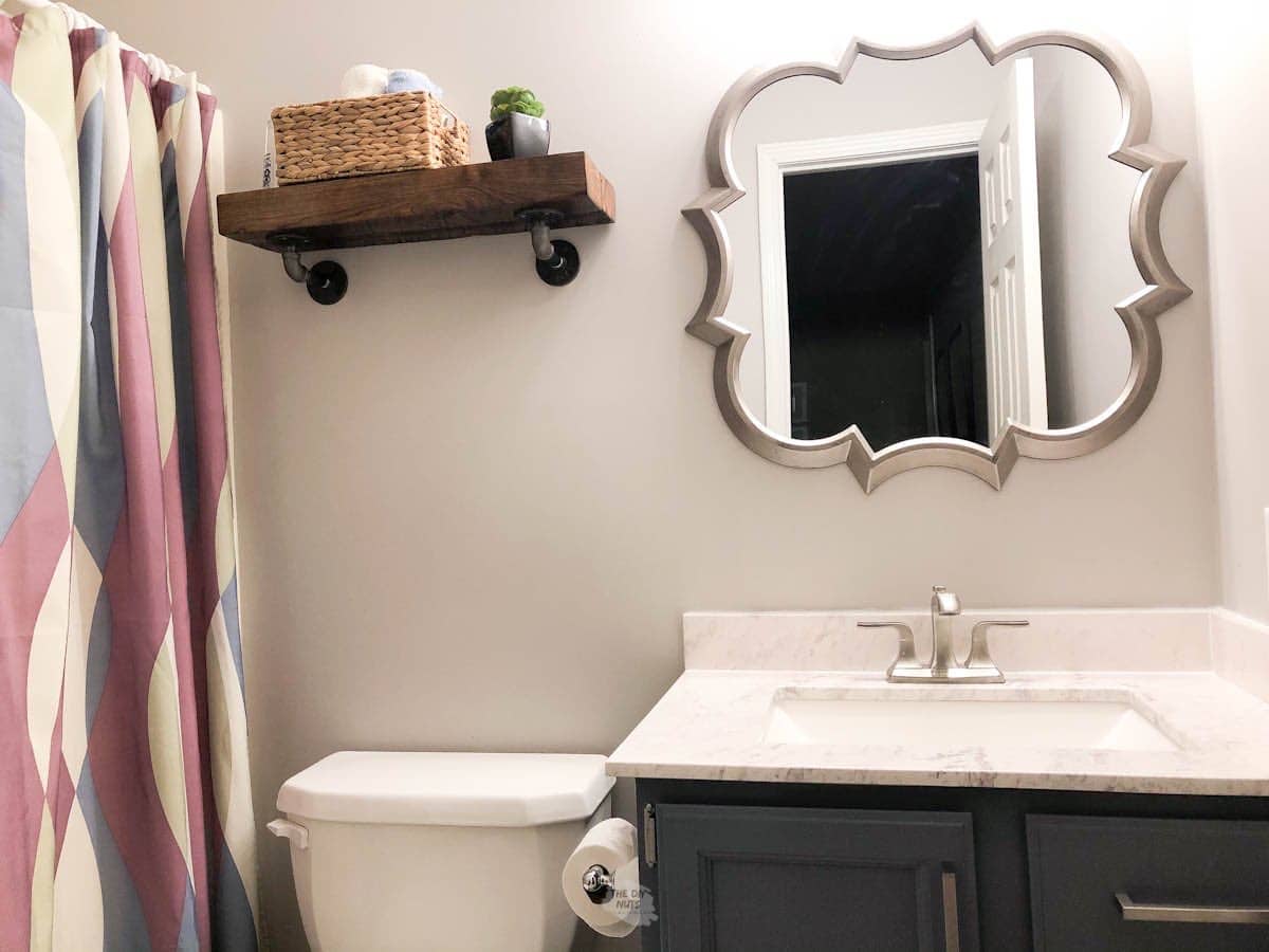 small bathroom with organic mirror, painted cabinets and industrial shelf over toliet.