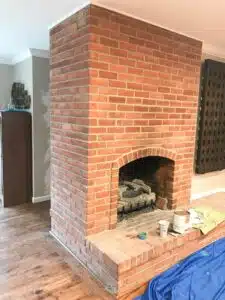 red brick fireplace with paint supplies sitting on hearth.