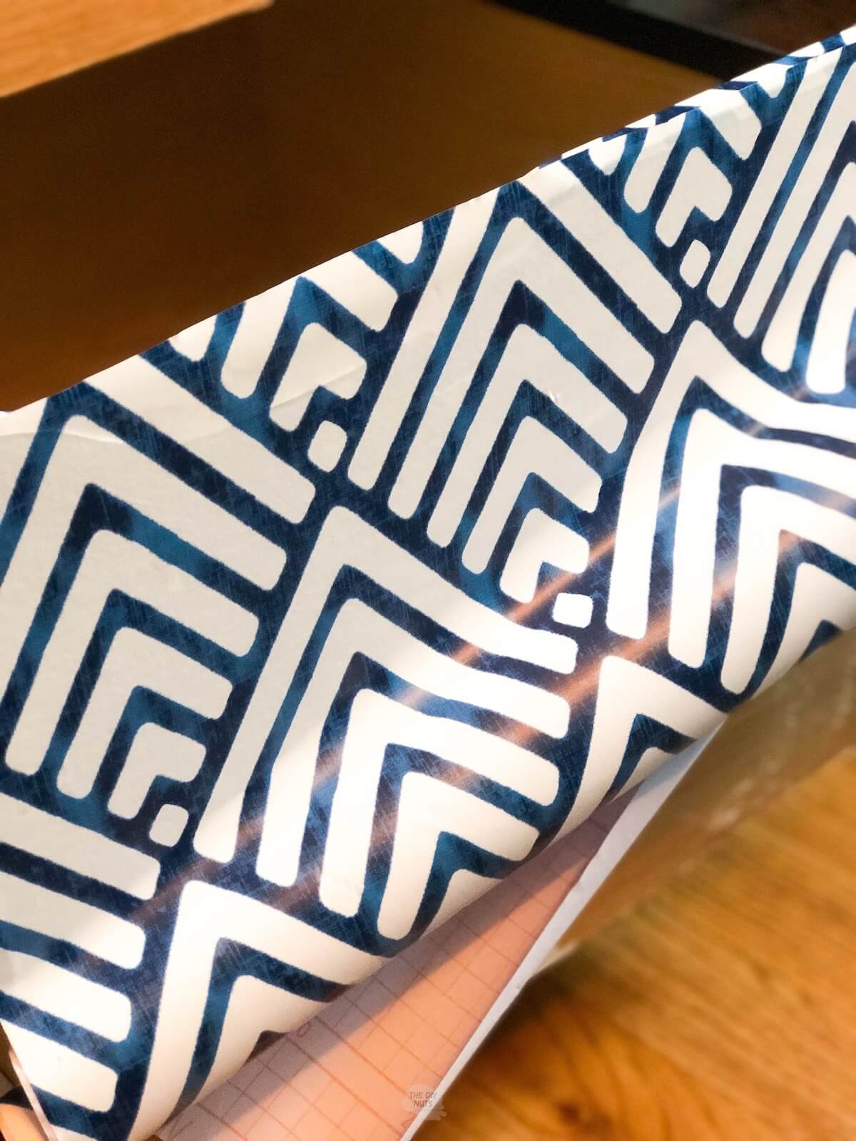 blue and white patterned contact paper partially stuck on wood.