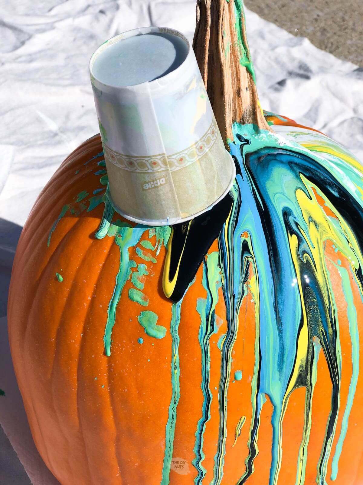 Cup left on pumpkin to pour paint on pumpkin to create a cool DIY painted pumpkin.