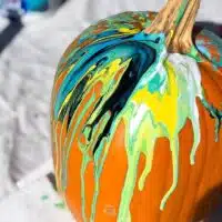 pumpkin with paint pour acrylic paint in teal, yellow, white and black paint.