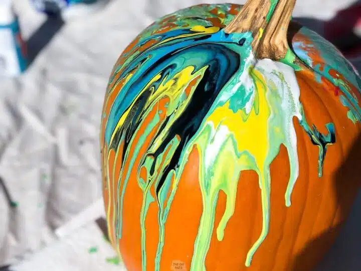 pumpkin with paint pour acrylic paint in teal, yellow, white and black paint.