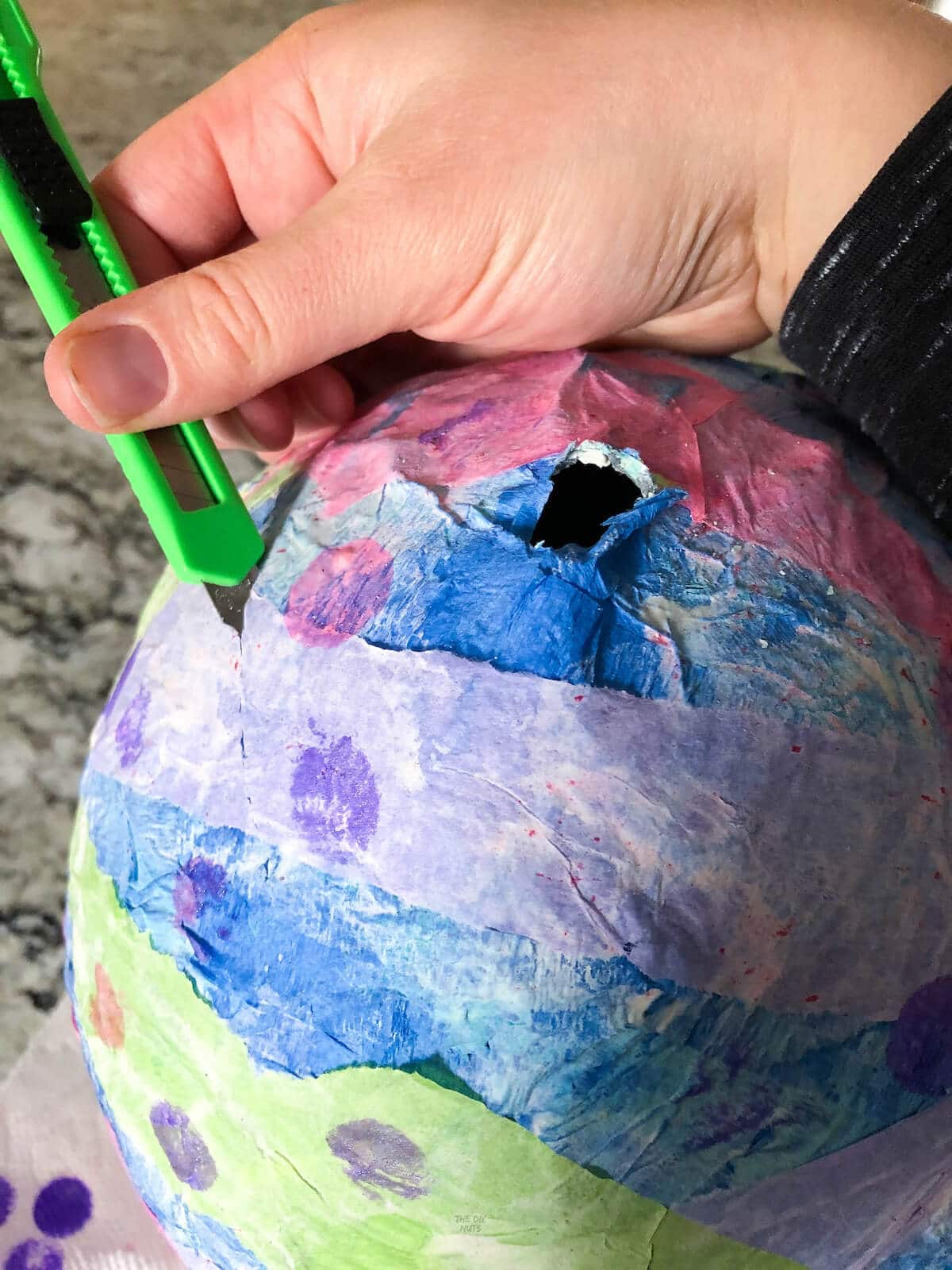 hand holding exacto knife cutting into paper mache piñata.