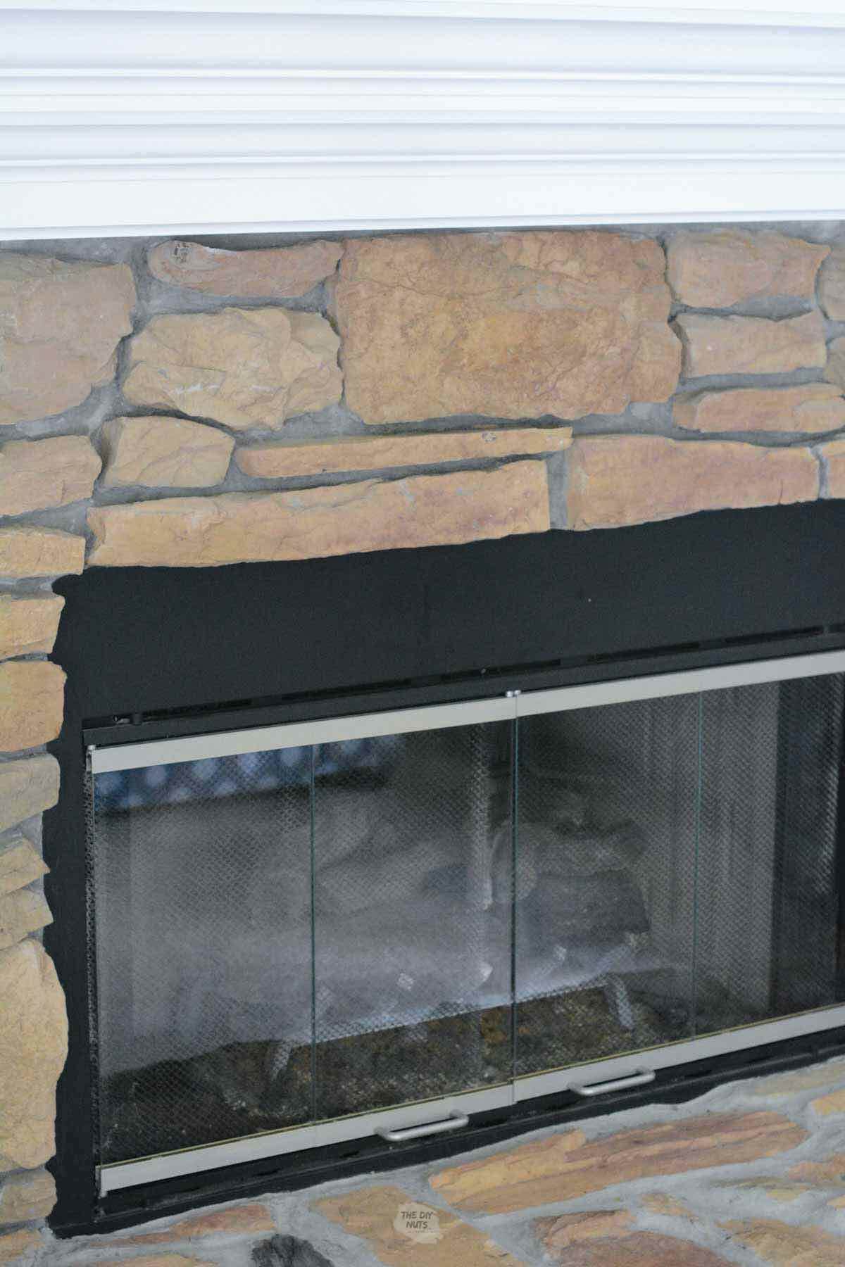 Silver metal and black fireplace cover and DIY white painted mantel with brown stone fireplace.