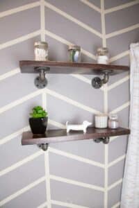 industrial pipe shelving with accessories with painted herringbone design on wall.