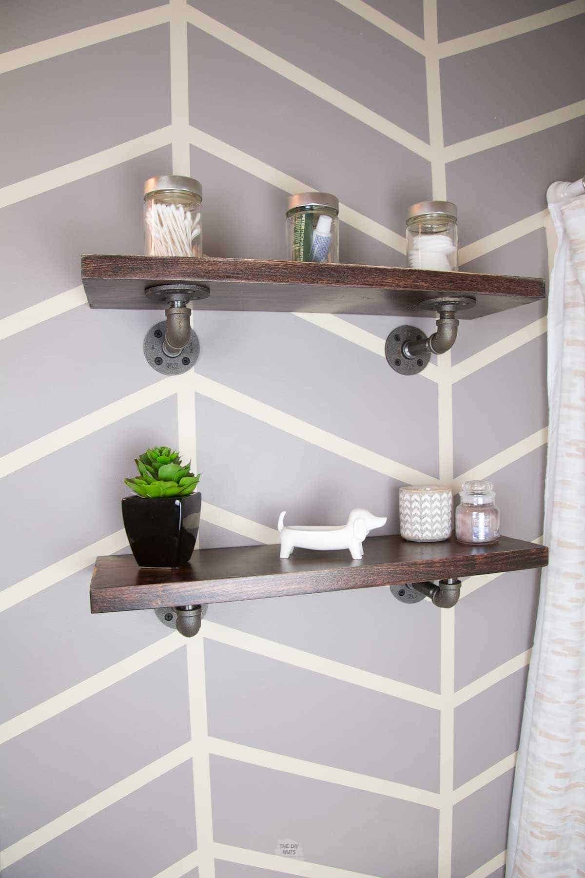two stained shelves on bathroom wall with grey herringbone painted pattern.