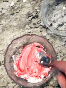 hand using a spoon to mix red food coloring in corn starch lotion dough.