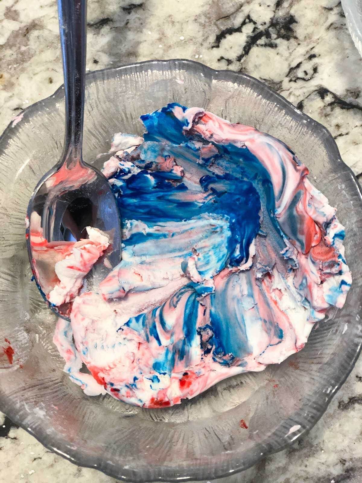 blue and red tie dye looking homemade playdough in small glass bowl.