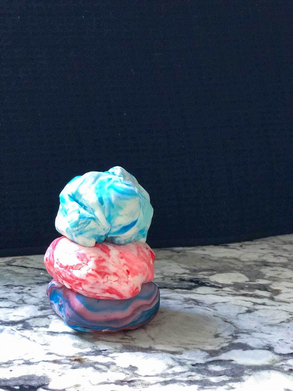 tie dye looking playdough in 3 balls on counter top.