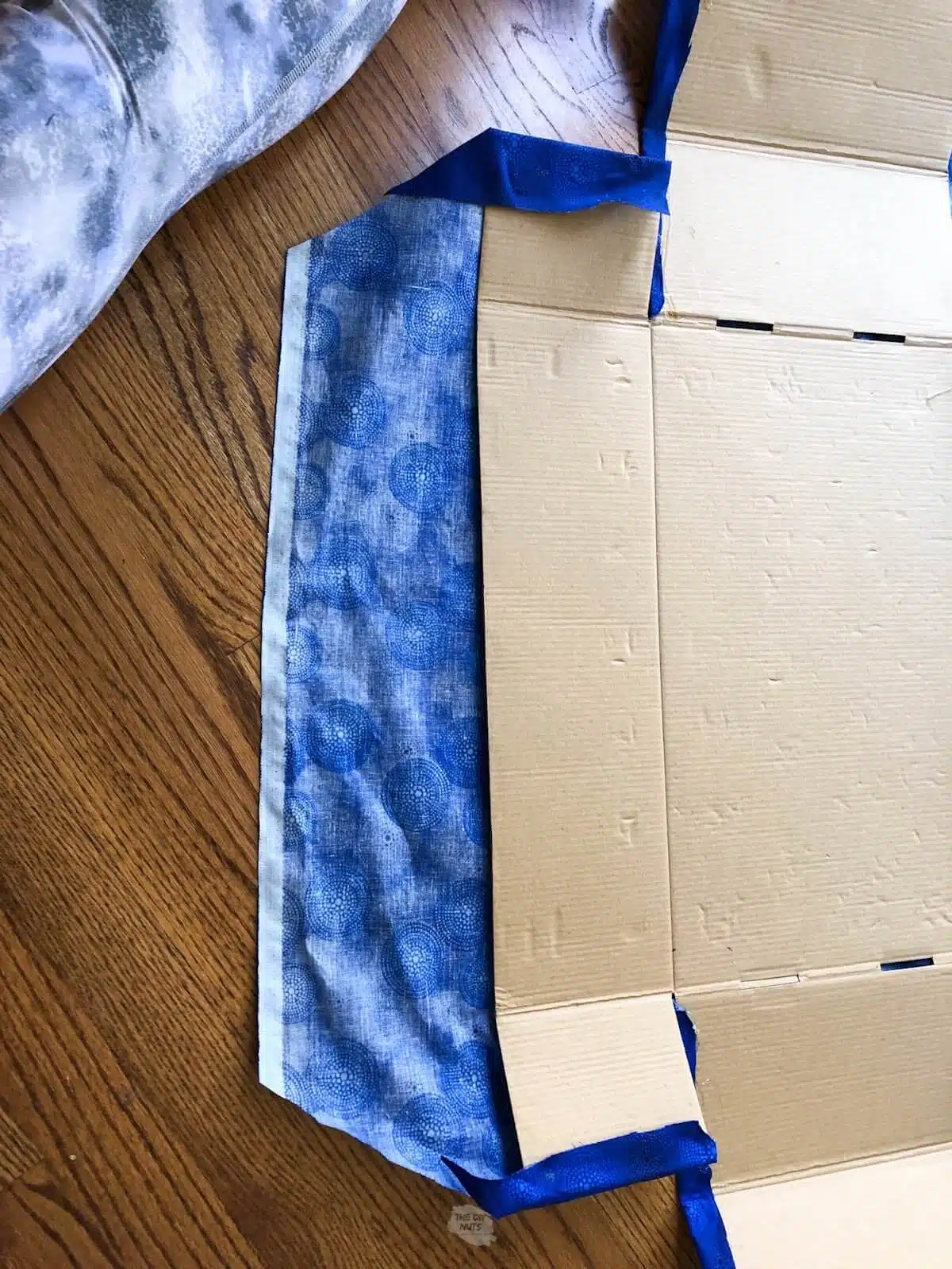 fabric being wrapped around edges of open cardboard box.