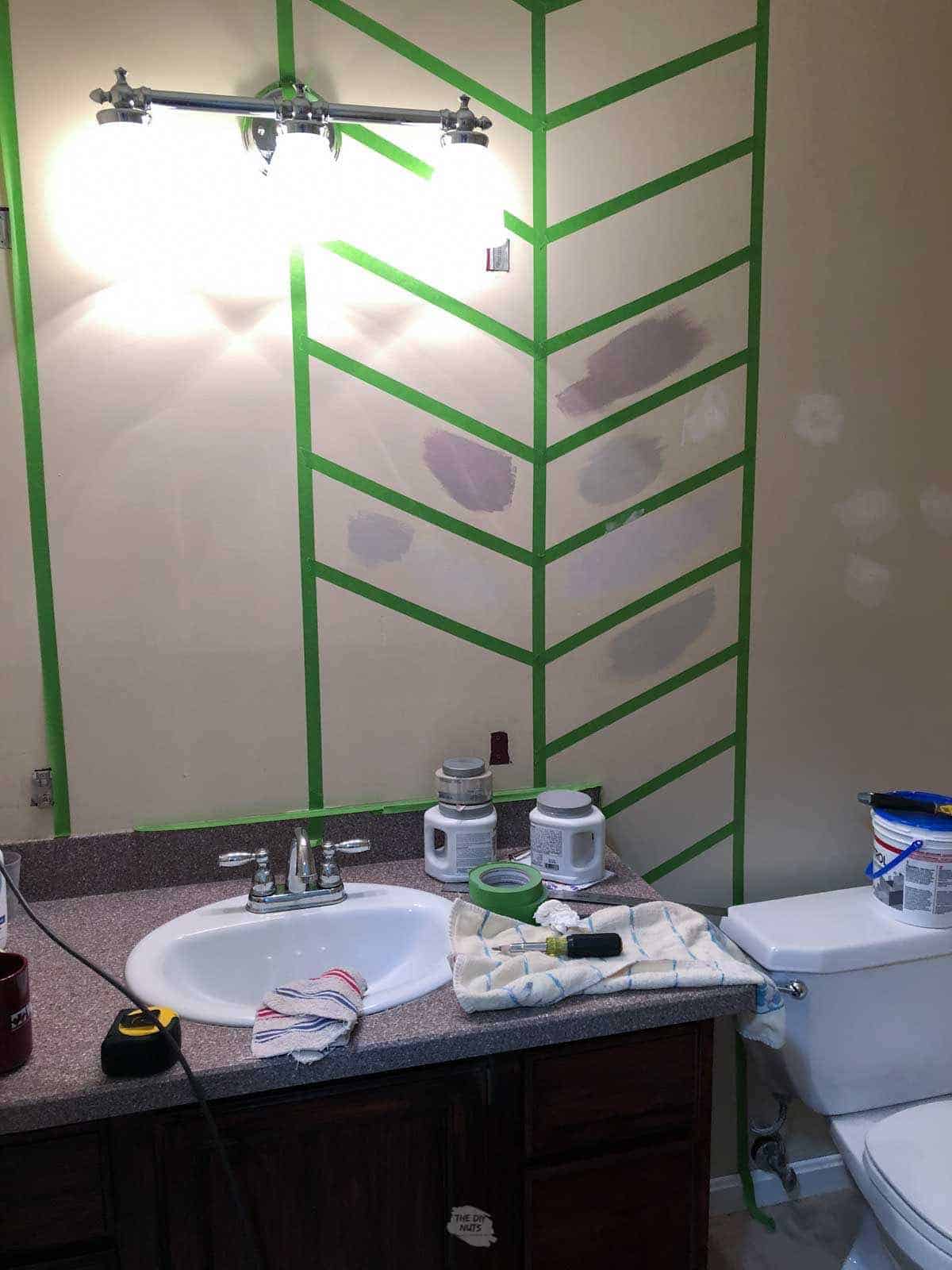 herringbone design tape on the bathroom wall with green tape and paint samples.