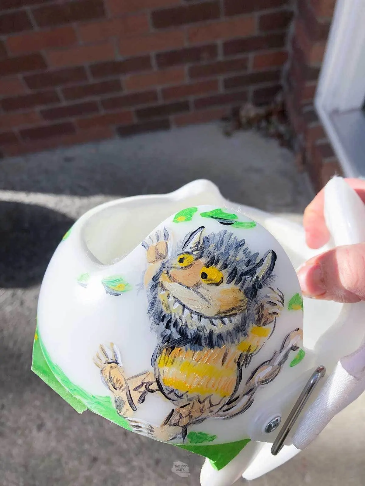 hand holding baby helmet with wild thing monster painted on the side.