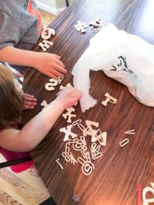 two preschoolers picking out wooden letters on brown table.