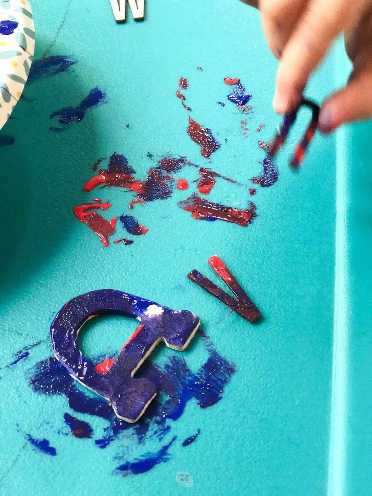 kids hand holding wooden letter with paint on a "d" on a teal table.