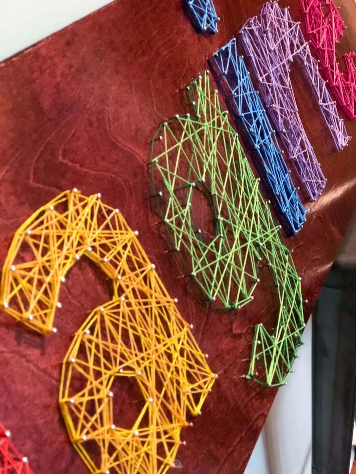 up close view of string art seeing yellow a, green g, blue i and purple n.