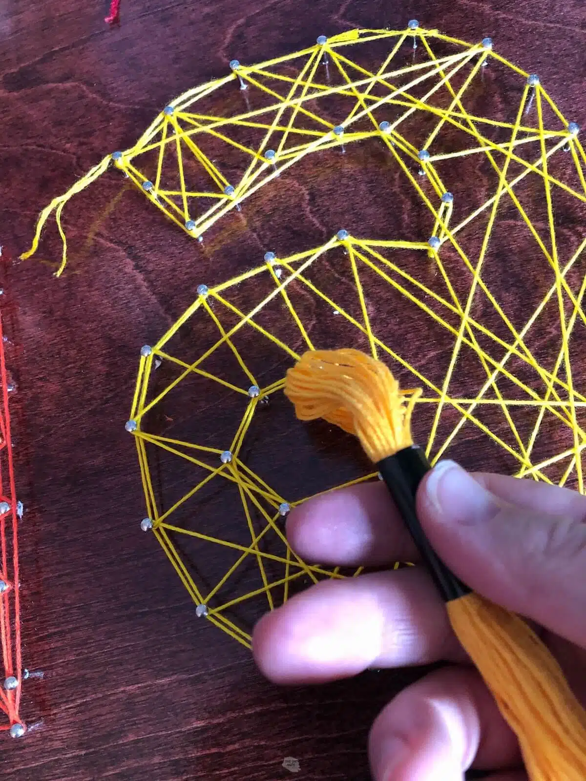 hand holding skein of yellow string in front of string art.