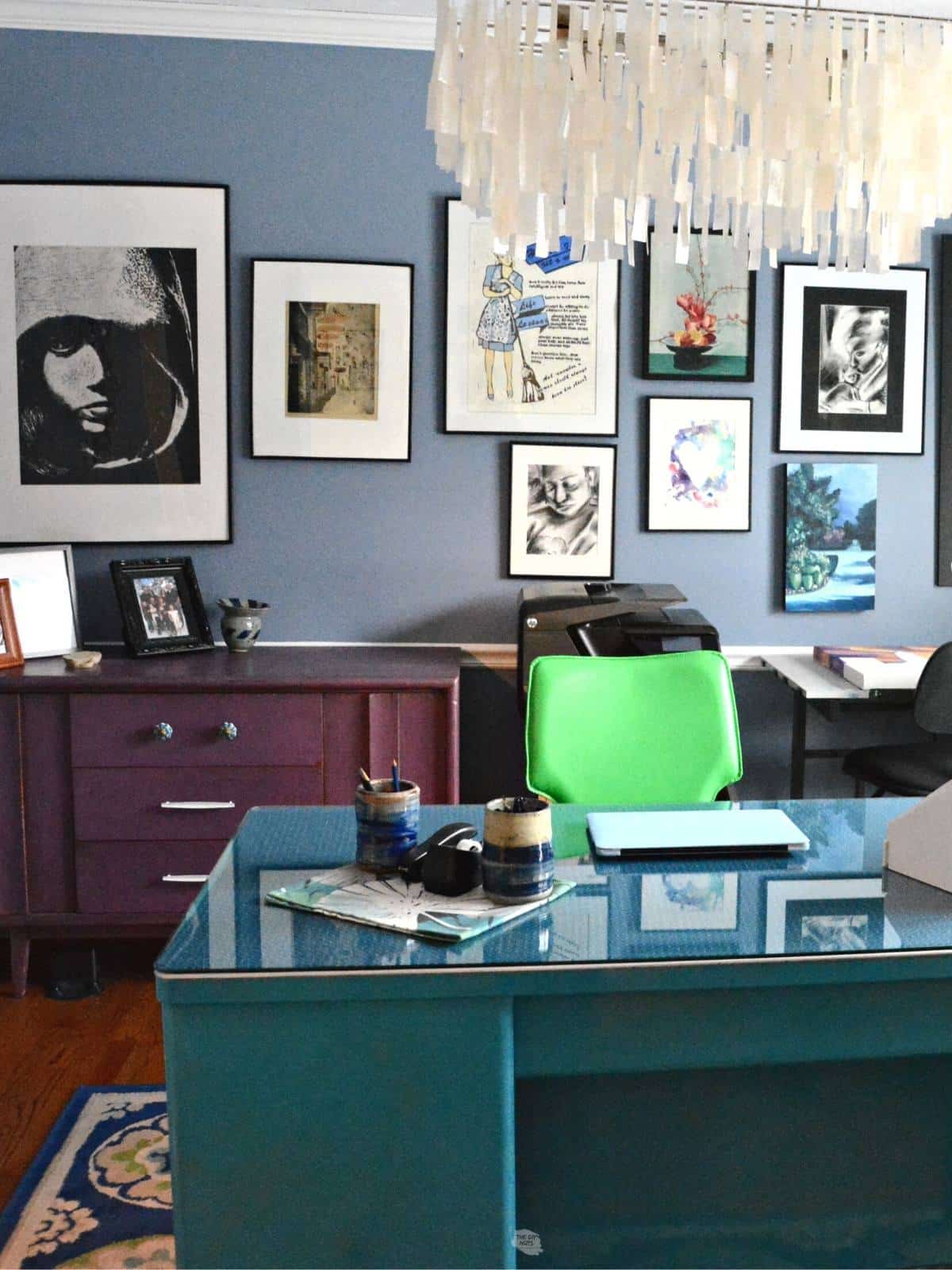 green desk chair and teal metal desk with artwork on the wall.